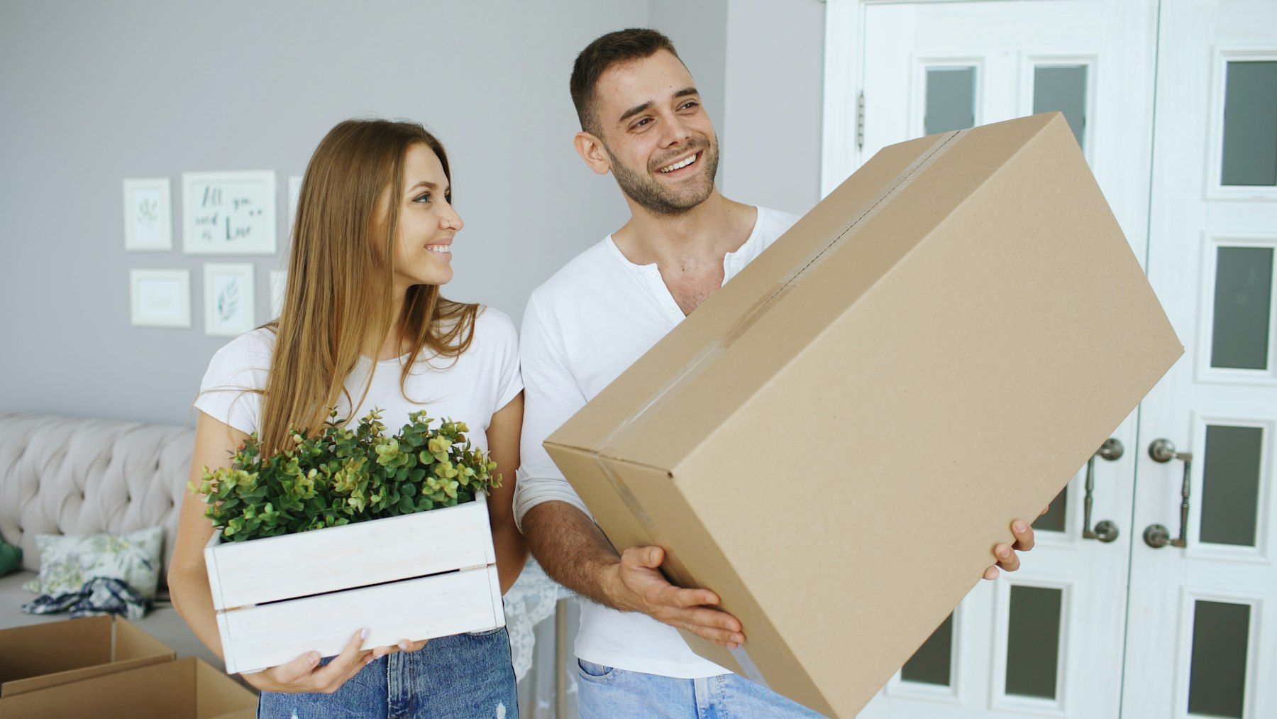 Couple carrying a cardboard box and a plant into their home
